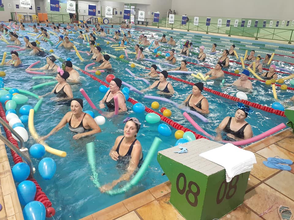 Pracegover: Fotografia. Aula de hidroginástica. Muitos alunos em uma piscina seguram aquatubes e fazem exercícios.